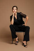 Seated on black chair, legs crossed, boss energy